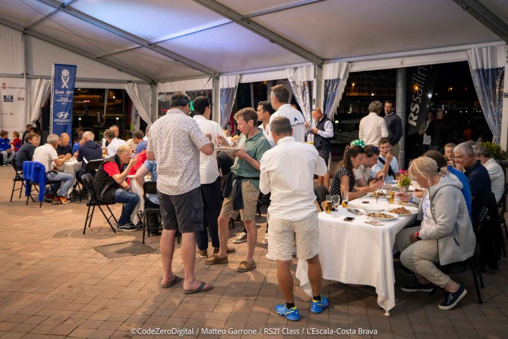 3. Serve Food with Plastic-Free Dinnerware<br>No plastic dinnerware, glassware, or cutlery was used for any meals during the 2024 RS21 World Championship. For daily meals, the opening ceremony, and the closing ceremony, we used compostable plates, wooden forks, paper napkins, and recyclable cardboard cups. During the opening ceremony and the awards ceremony, cava (a typical local beverage) was served in glass flutes. For the crew dinner, ceramic plates, glassware, and metal cutlery were rented.