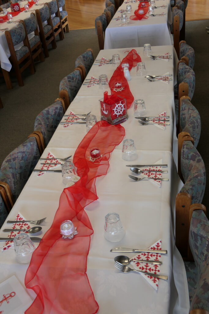 3. Serve Food with Plastic-Free Dinnerware<br>3. Gulf Harbour Yacht Club has always used plastic-free beverage glasses, china, and cutlery for its food and bar services.During the 2025 WOWW event, we reaffirmed the club’s commitment to plastic-free food and bar service with caterers and volunteers. Morning coffee service was supplied with china mugs, metal teaspoons, and china cream pitchers. (Photo 3a) China plates and bowls, and cloth tablecloths, were used for all food service. (Photo 3b) Lunches on participating boats were  provided in bags made of hessian with paper labels and cotton strings. Sandwiches were wrapped in wax paper and fresh fruit required no wrapping. Prizegiving Night tables were set with linen tablecloths, real glasses, metal cutlery and small paper napkins which were composted after use. Centerpieces were reused. (Photo 3c) Ends of roll paper from printing were repurposed on top of buffet tablecloths to reduce the number of times they needed to be laundered. (Photo 3d)