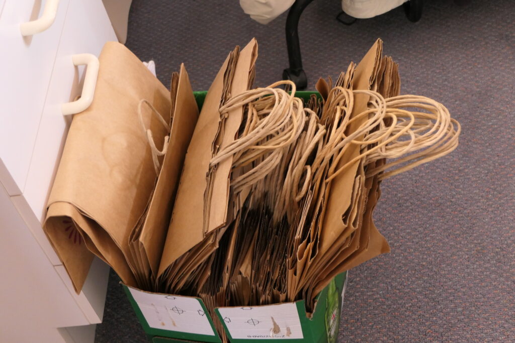 4. Skip Bags or Go Reusable<br>4. On the water sailing events require many supplies and pieces of equipment to be tranferred to yachts by boat owners, yacht club organisers, race crew, and skippers. Without reusable totes or recycled bags, waste could easily get out of hand. The WOWW Green Team made sure that reusable bags and totes were available for the multiple trips to boats, vehicles and the club. (Photo 4a) Packed lunches on boats were provided in bags made of hessian with paper labels and cotton strings. Sandwiches were wrapped in wax paper and fresh fruit required no wrapping. Crews were asked to return all waste/rubbish in the bags, to be disposed of appropriately back at the clubhouse. A bonus came with the use of bags marked with the brandname of Evolution Sails, the 2025 Gold Sponsor. (Photo 4b)
