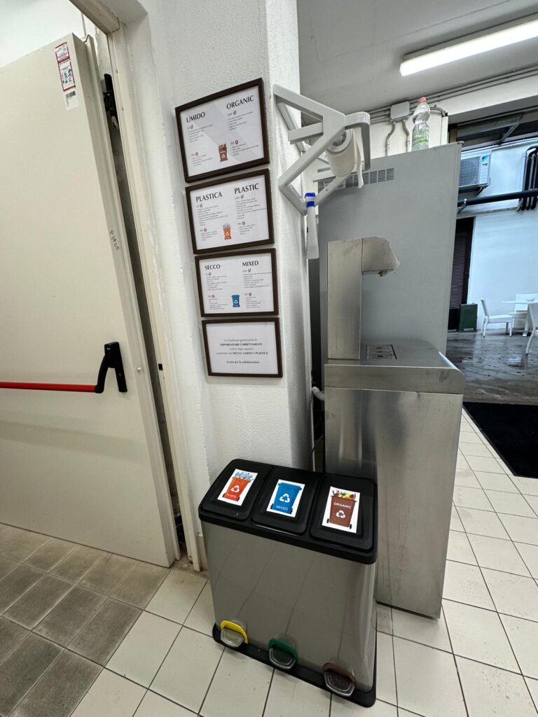 8. Post Educational and Reusable Signage<br>Bins and information on how to differentiate have been placed in the media room and media centre, each with a sign clearly indicating what type of waste should be put in them.
Next to the drinking water fountain is a noticeboard displaying statistics that prompt reflection on sustainability: the average number of litres of water consumed per day in Europe, the average daily consumption in Italy, the tonnes of plastic that end up in the Mediterranean Sea every year, and the number of animal species affected by pollution.
