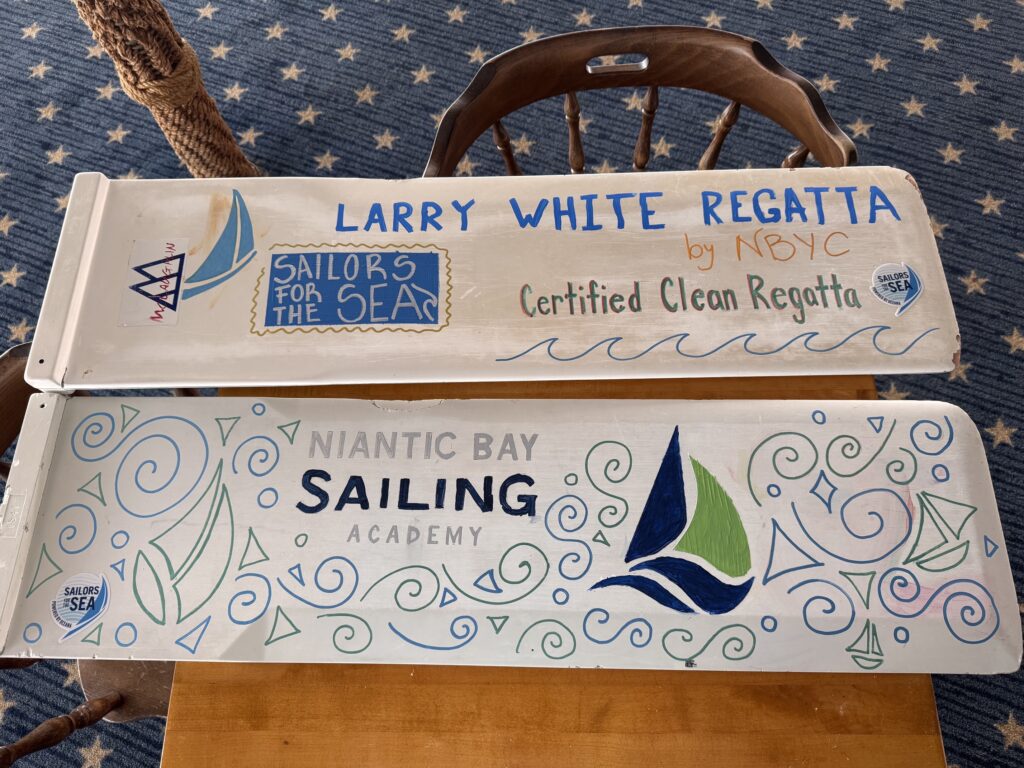 8. Post Educational and Reusable Signage<br>Youth green team members Olivia Murin and Kennedy Nemec created a colorful sign on a whiteboard that lists clean regatta practices. Kids from beginner sailing classes at NBSA also helped to create signage from recycled materials, such as old optimist centerboards and scrap wood found in the water. 